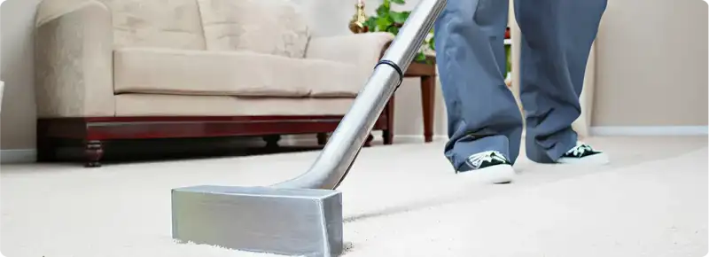 Carpet cleaning technician using a hot-water extraction wand on a light-colored carpet in a living room, Boulder, CO.