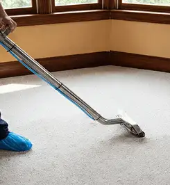 Steam carpet cleaning technician using a hot-water extraction wand on a residential carpet, wearing blue protective shoe covers Boulder, CO.