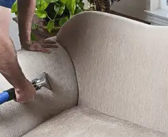 Professional upholstery cleaner deep-cleaning a fabric sofa with a handheld extraction tool and hose in Boulder, CO.